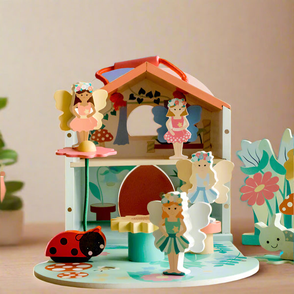 Wooden fairy house with fairy figurines and accessories on a decorative table.