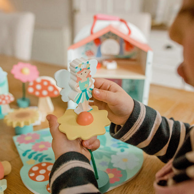 Child playing with a toy fairy set on a wooden floor